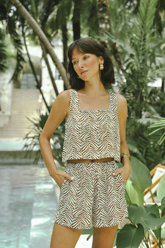 Woman in a patterned outfit standing by a pool with greenery in the background