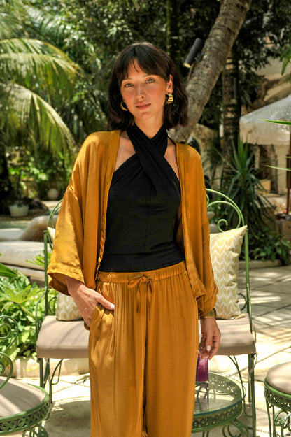 Woman in mustard cardigan and black top standing in a tropical outdoor setting