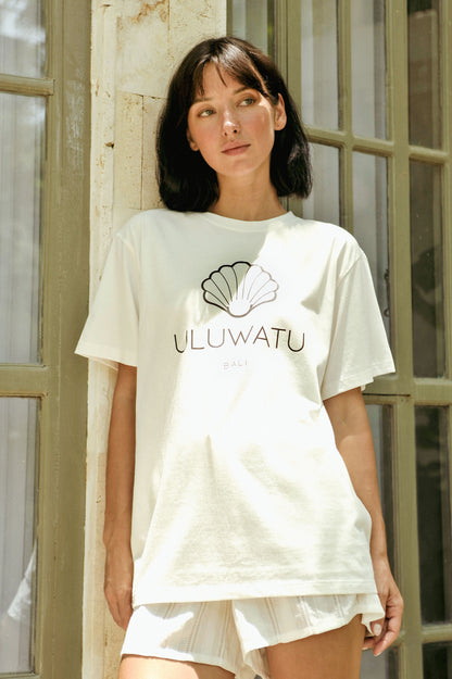 Woman wearing a white t-shirt with 'ULUWATU' logo in front of a glass door.