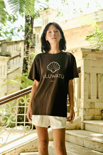 Person wearing a black t-shirt with 'VLUWATU' logo outdoors.