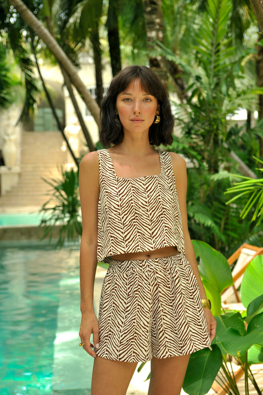 Woman wearing a patterned outfit standing by a pool with greenery in the background