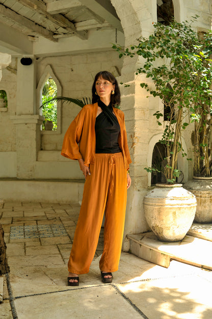 Woman in a mustard yellow outfit standing in an outdoor setting with plants and stone architecture.