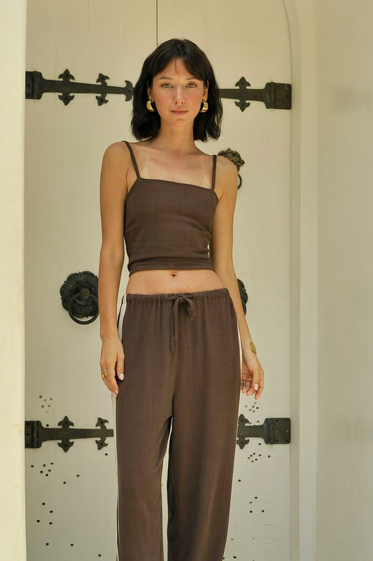 Woman wearing a brown top and pants standing in front of a decorative door.